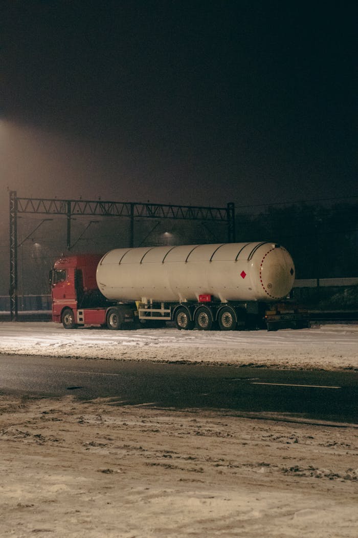 Red truck with tanker parked on snowy road at night in Bydgoszcz, Poland.